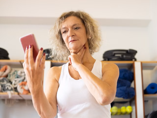 Middle-aged woman checking pulse on smartphone during fitness routine indoors.