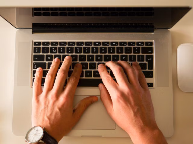Hands typing on a laptop keyboard, showcasing a modern workplace environment with a mouse nearby.